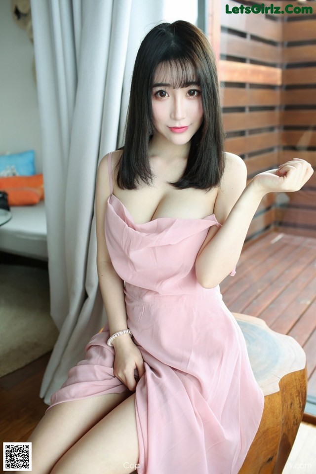 A woman in a pink dress sitting on a wooden bench.