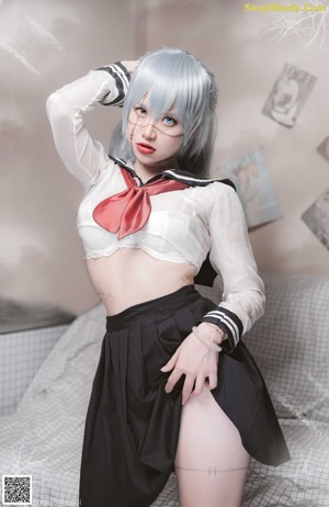 A woman in a white shirt and black skirt sitting on a bed.