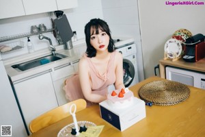 A woman sitting on top of a wooden table next to a cake.