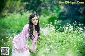 A woman in a white dress sitting on the ground in the woods.