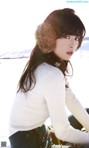 A young woman wearing a fur hat sitting on the ground.