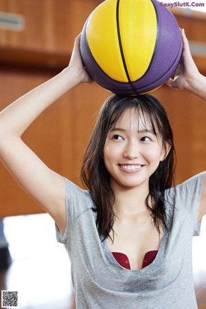 A young woman holding a volleyball on a basketball court.