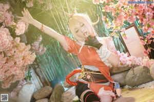 A woman in a kimono sitting under a tree with pink flowers.