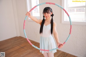 A young girl in a white leotard and blue skirt holding a hula hoop.