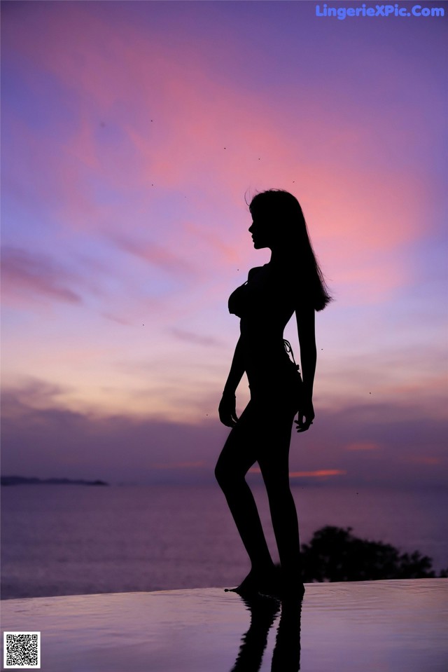 A silhouette of a woman standing on the edge of a swimming pool.