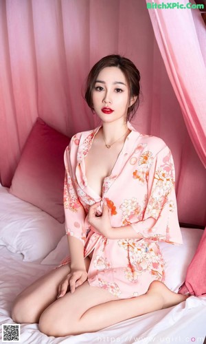 a woman sitting on top of a bed in a pink robe