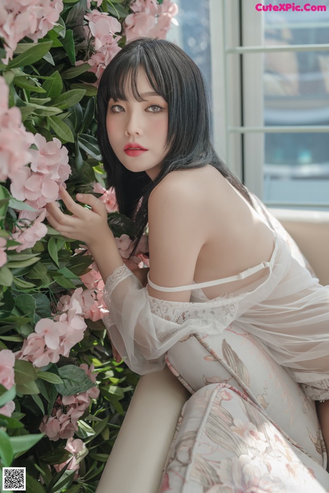 A woman in a white dress sitting in front of pink flowers.