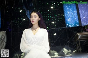 A woman in a white robe holding a shower head.