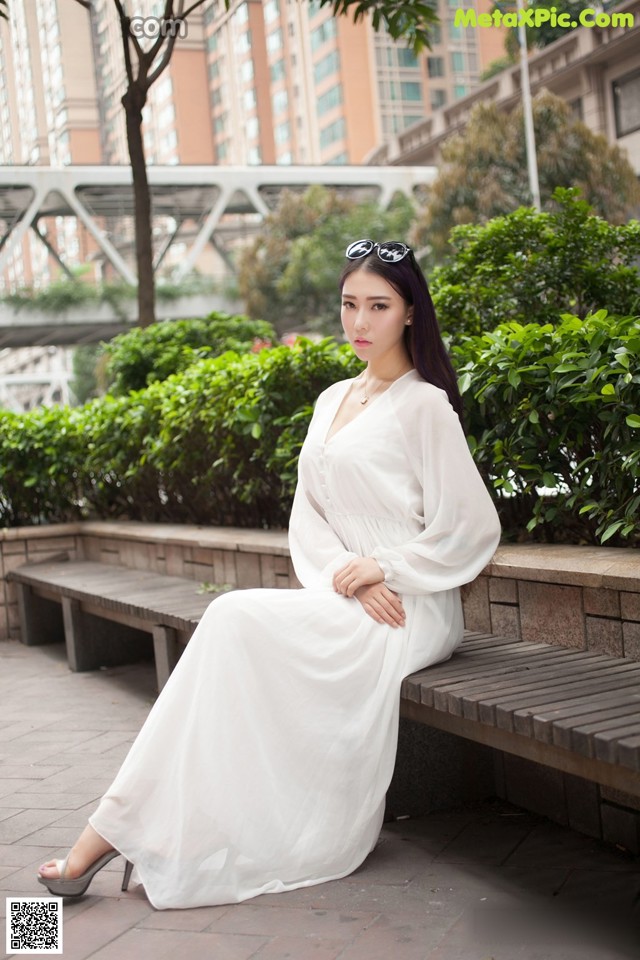 A woman in a white dress sitting on a bench.