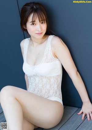A woman in a white lingerie sitting on a wooden floor.