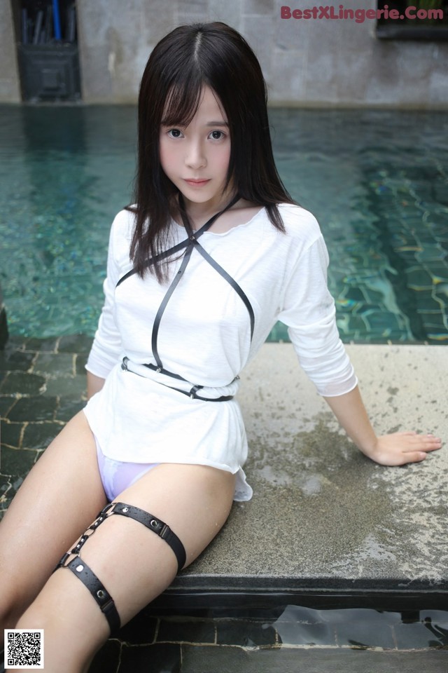 A woman in a white shirt and black stockings sitting by a pool.