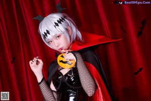 A woman in a black and red outfit holding a pumpkin.