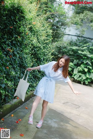 A woman in a blue and white striped dress holding a white bag.