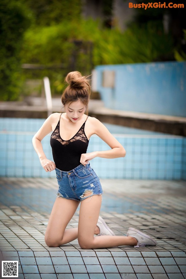 A woman in a black top and denim shorts by a swimming pool.