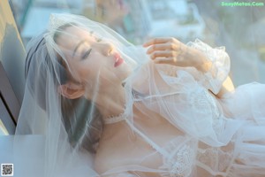 A woman in a white lingerie sitting on a bed.