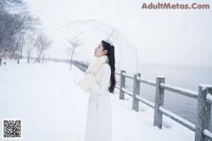 A woman standing in the snow holding an umbrella.