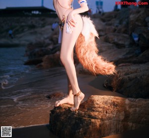 A woman in a bikini sitting on a rock on the beach.