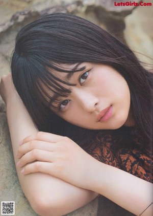 A woman with long black hair leaning against a wooden pole.