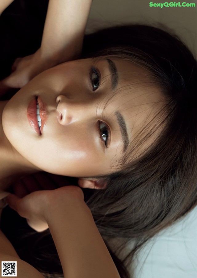 A woman laying on top of a bed with her hands on her head.